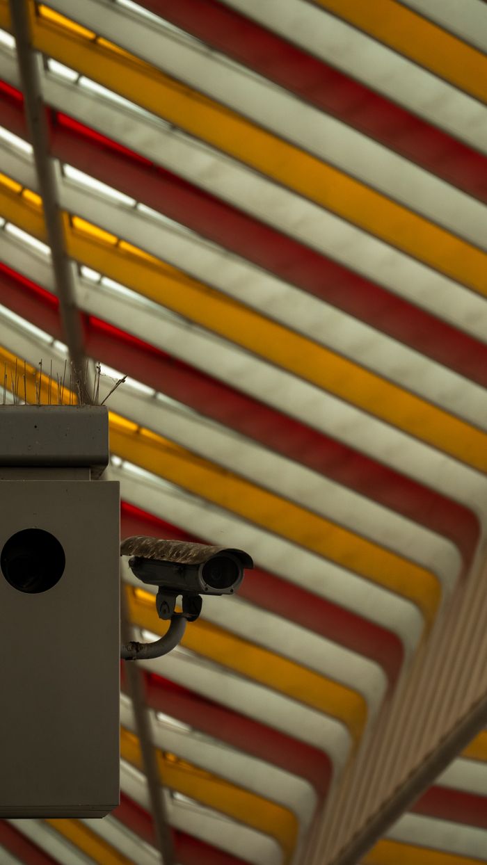 A security camera under a vibrant industrial ceiling with red and yellow stripes.